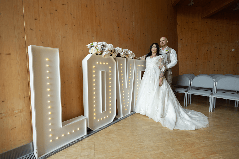 Bride and groom stood in front of large illuminated LOVE sign.